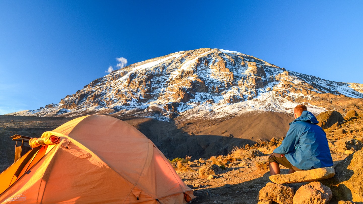 Evening view of Kibo with Uhuru Peak (5895m amsl, highest mountain in Africa) at Mount Kilimanjaro,Kilimanjaro National Park,seen from Karanga Camp at 3995m amsl. Tent and young hiker in foreground.