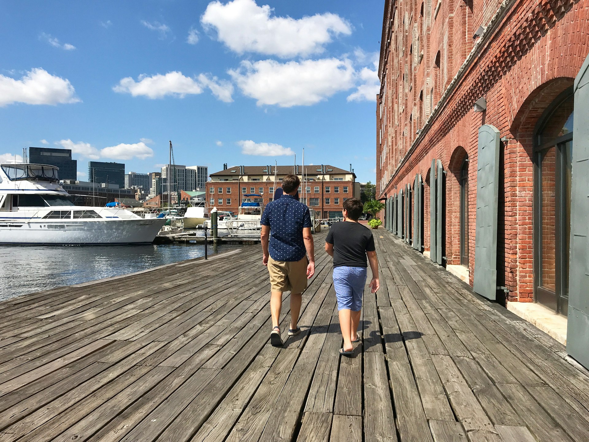 Father and son Walking along the Waterfront in Baltimore. There are a few large boats moored in the river. 