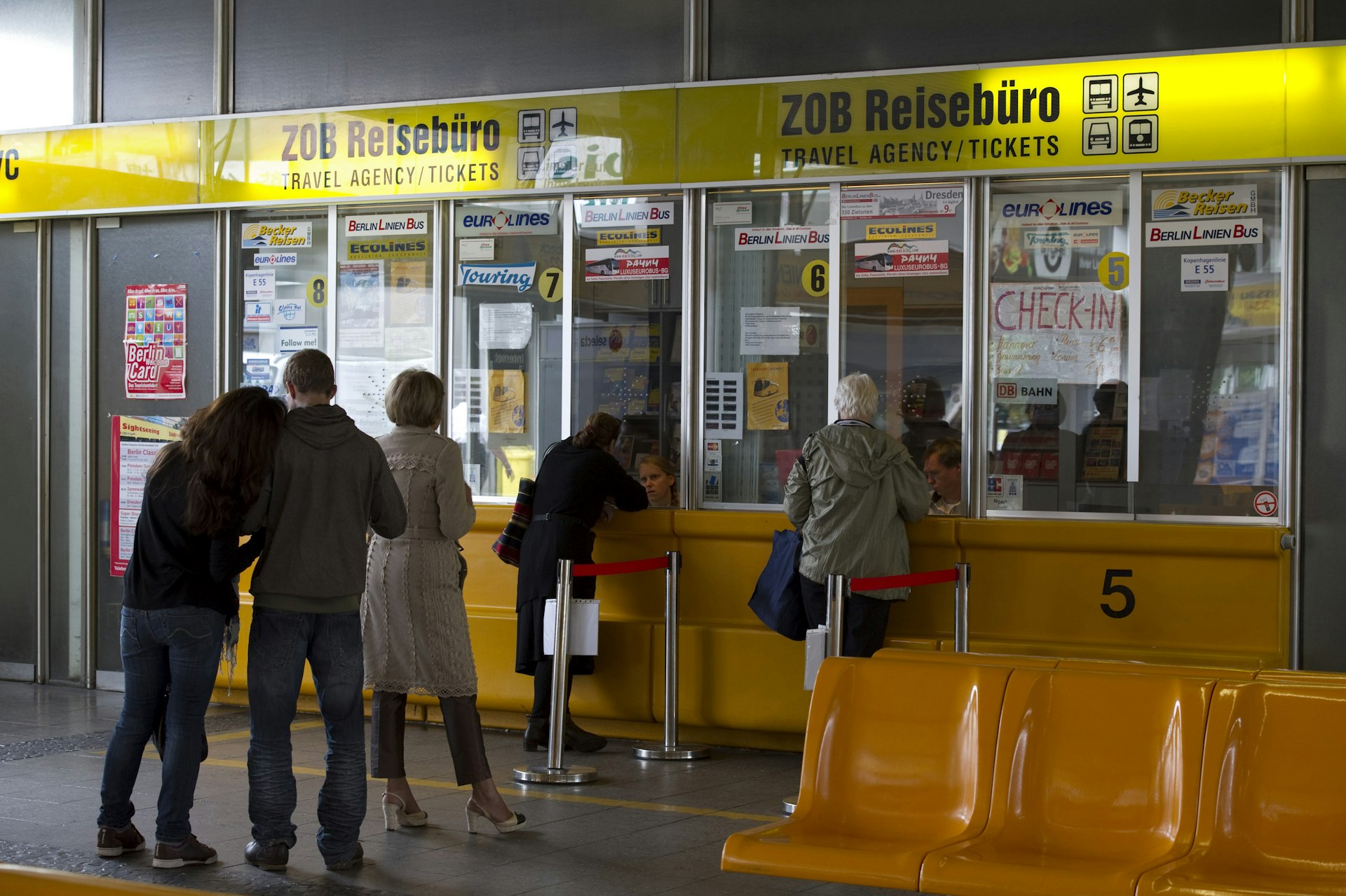 Passengers queue at a yellow ticket counter to purchase travel passes in Berlin