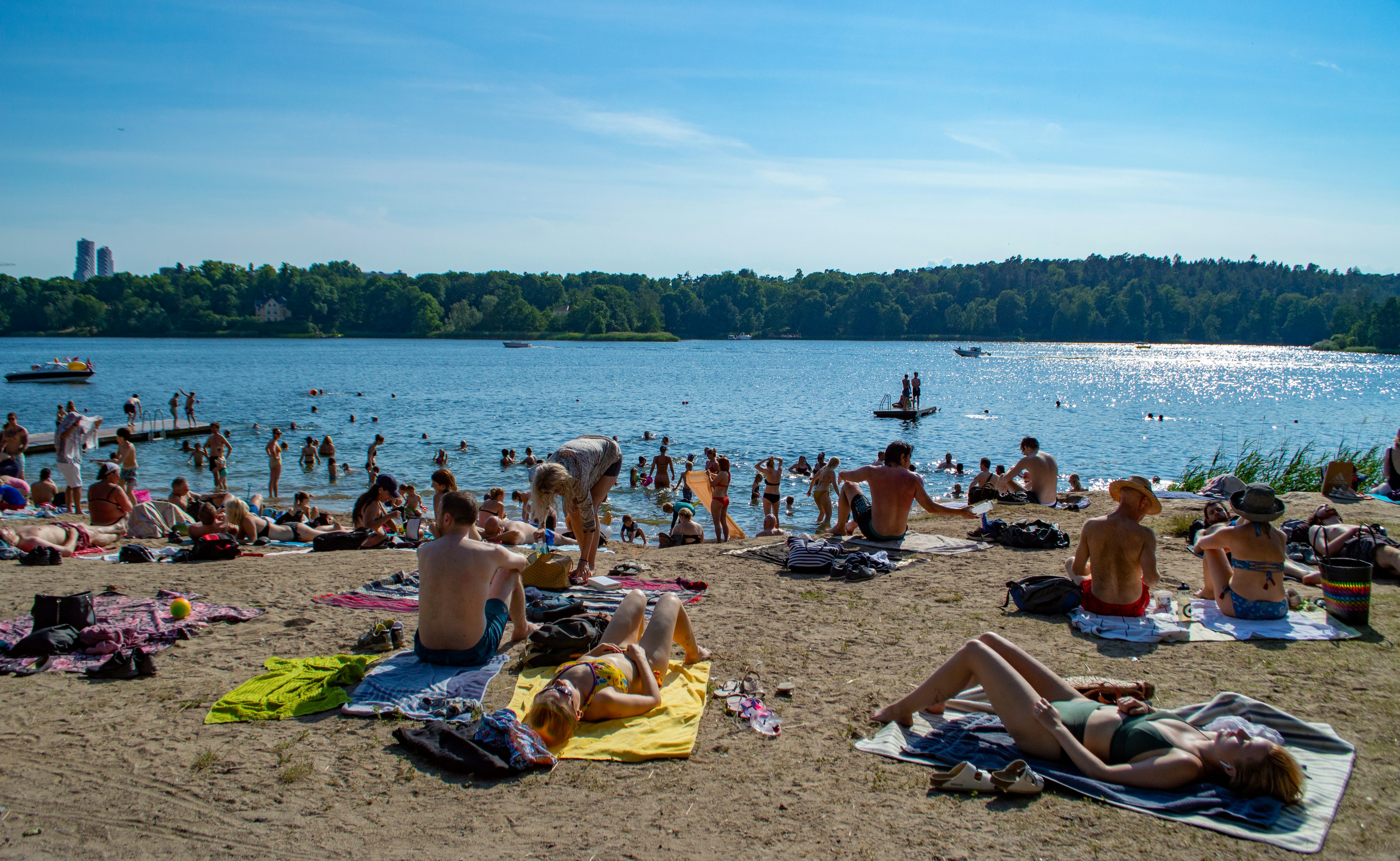 Lots of people laying on the sandy beach as kids play in the water. The sun is shining