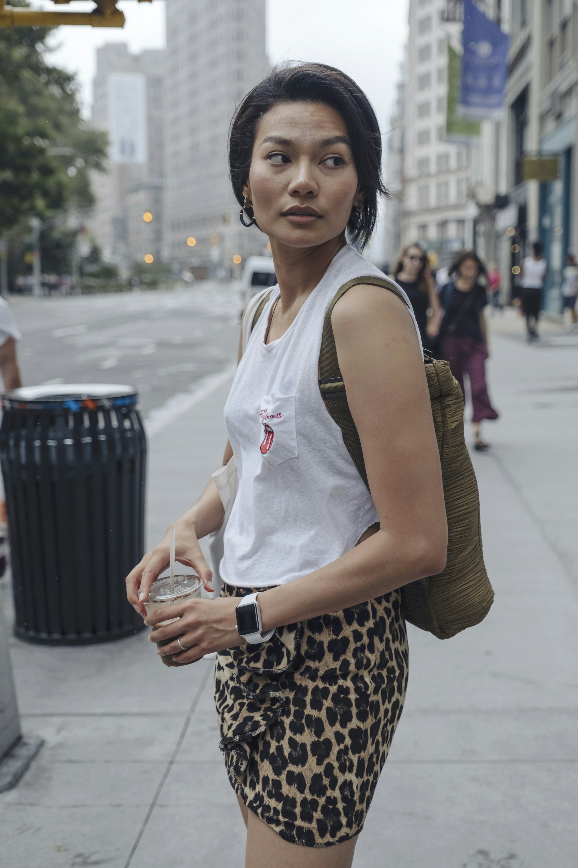 A woman wears a fitted white tank top and a short leopard-print skirt. A purse is dangling from her shoulder. 