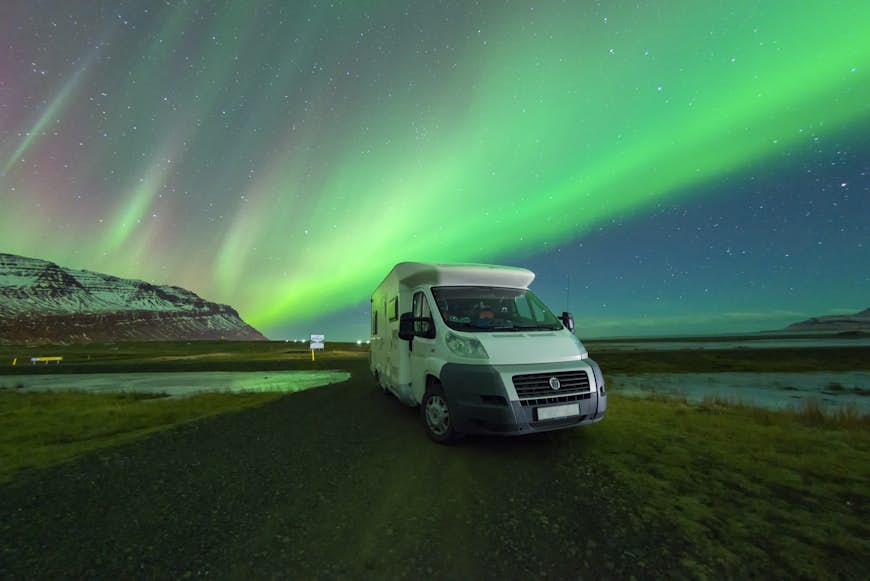 The northern lights appear in the sky above a campervan