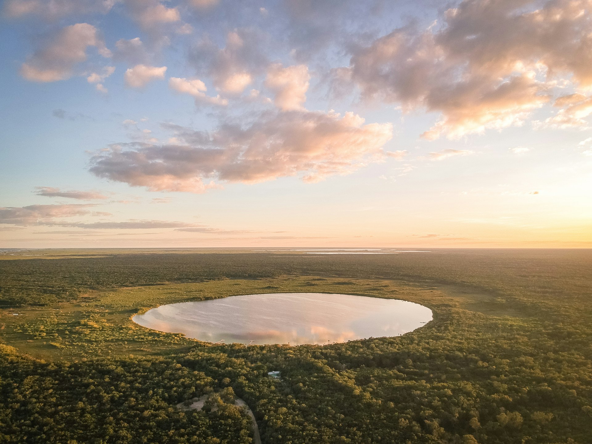 The sun sets over a perfectly circular lagoon surrounded by jungle