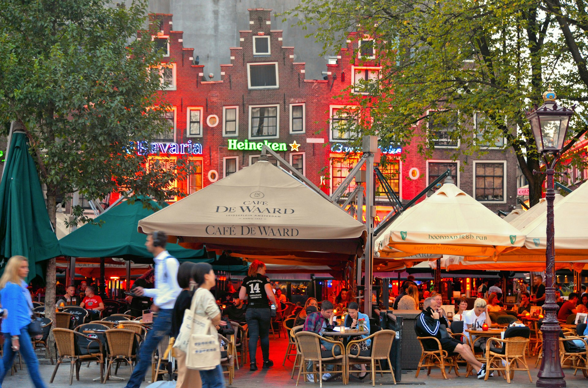 People sat outside at restaurants and bars under awnings in front of traditional Dutch buildings
