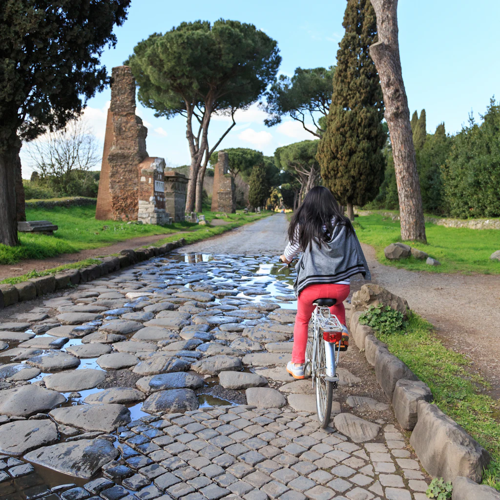 Riding a bike, Via Appia, Rome A woman rides a bike along a long cobbled road lined with trees