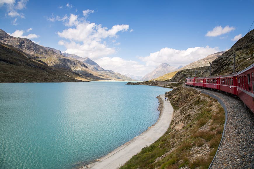 A red Bernina Express train travels along a lakeshore in Switzerland