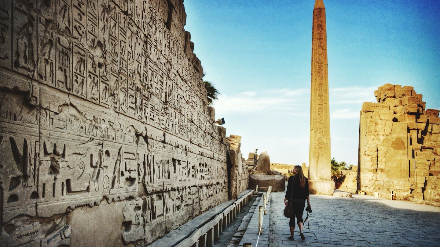 A woman walking past wall carvings at Karnak Temple.