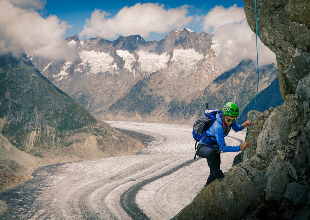 A rock climber works here way up a cliff face near the Aletsch Glacier. Behind, the glacier, which appears like a river of white ice, is clearly visible between the mountains.