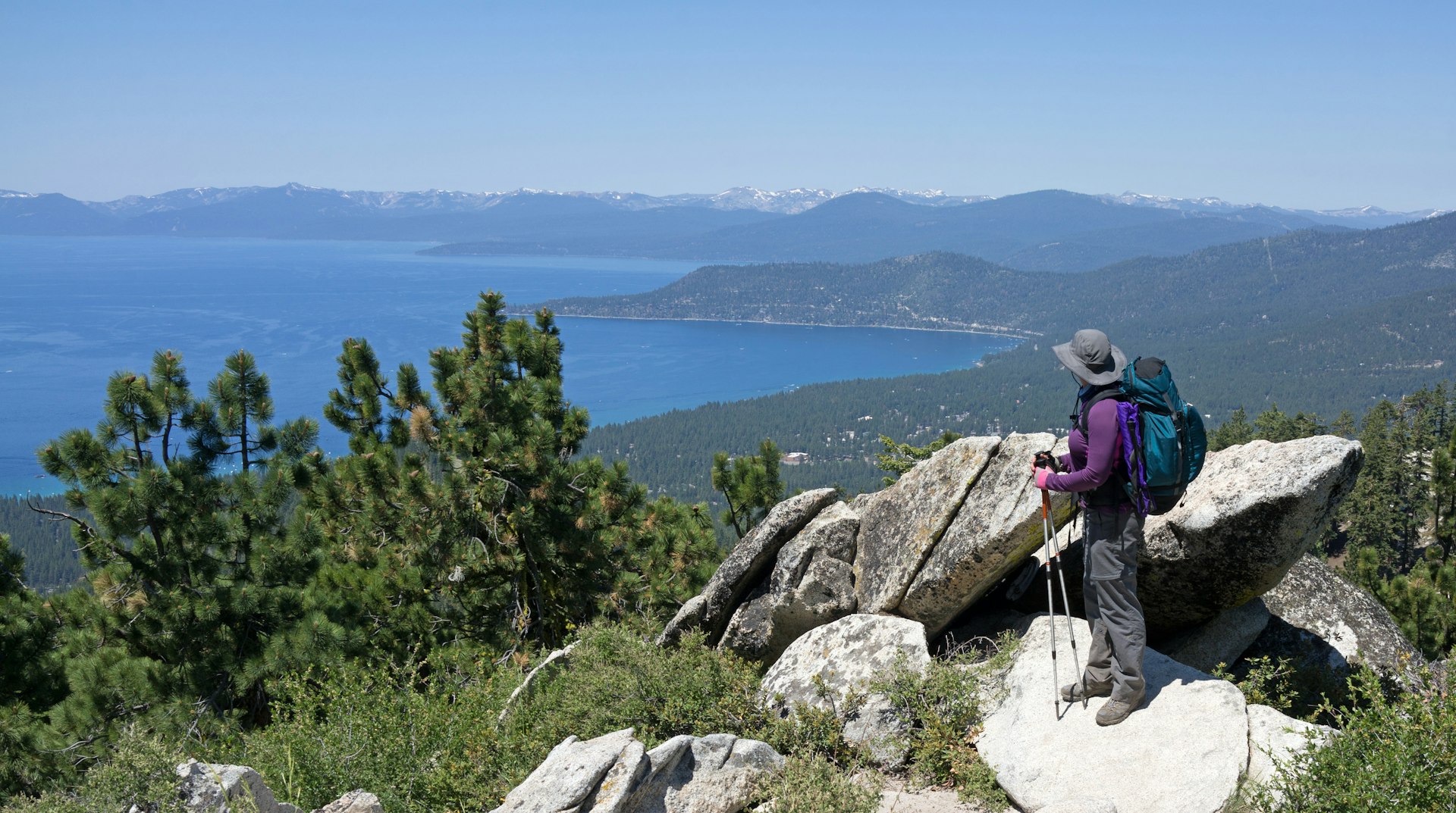 A hiker carrying a lot of gear pauses to look out over a lake view