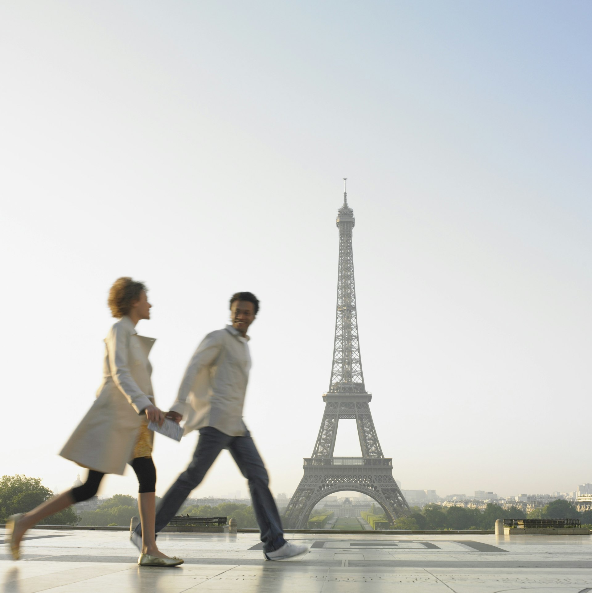 Two people walk hand-in-hand with a large iron pointed tower in the background