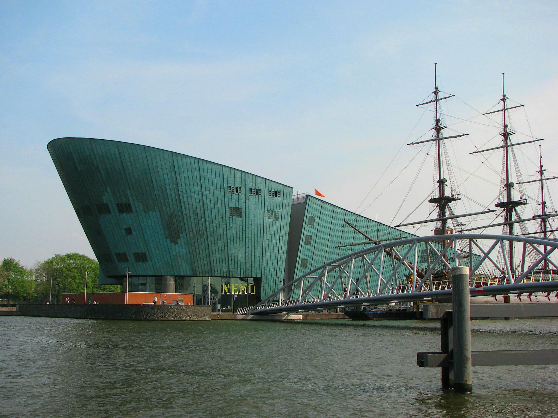 A large green copper hull-like building at the edge of the water