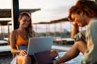 Mixed race girl and blonde girl on the beach using laptops during summer time vacation. Shot on Canon, 35mm lens iso 100. magic hour