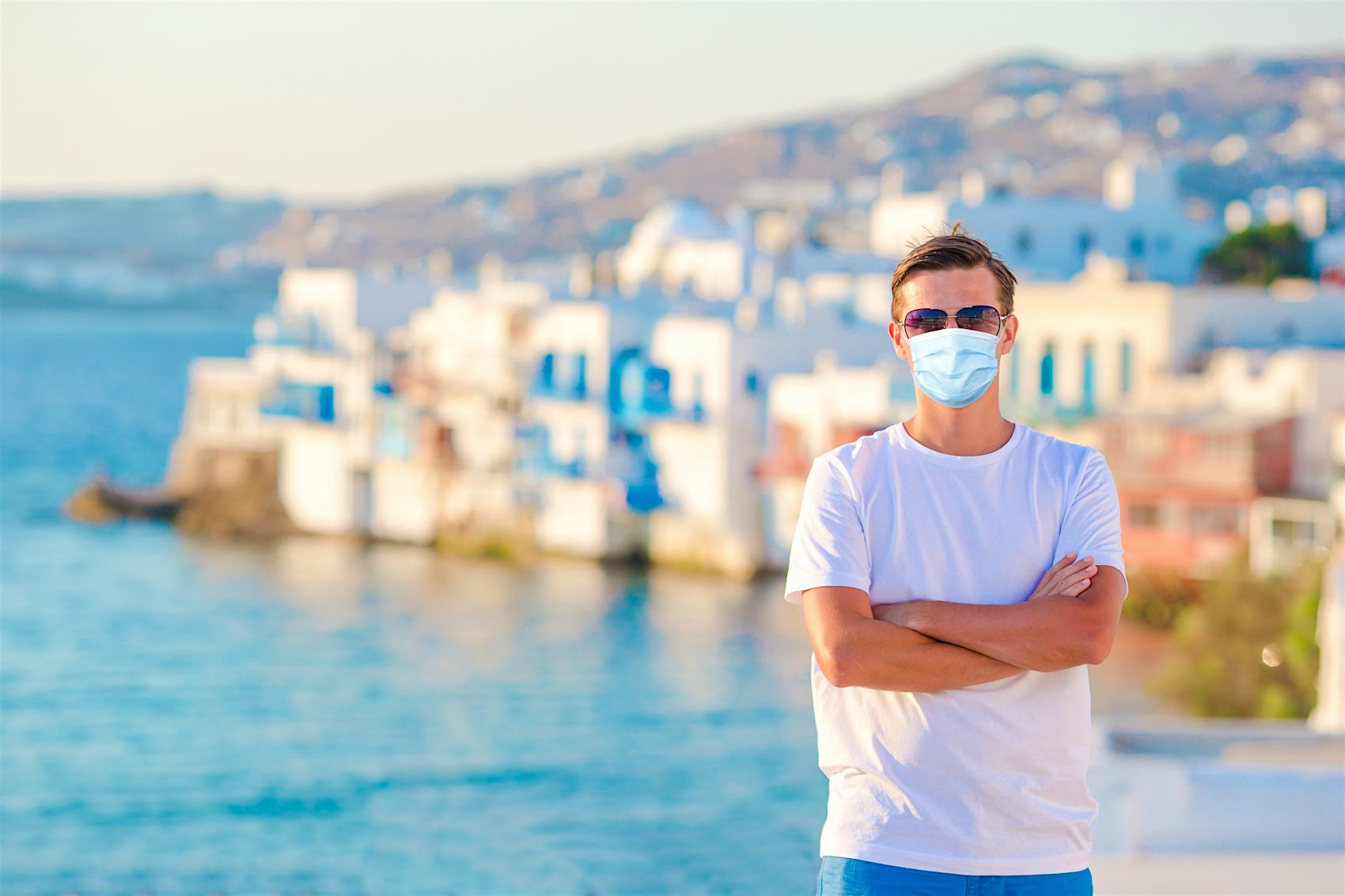 Masked person posing for image with coastal destination in the background