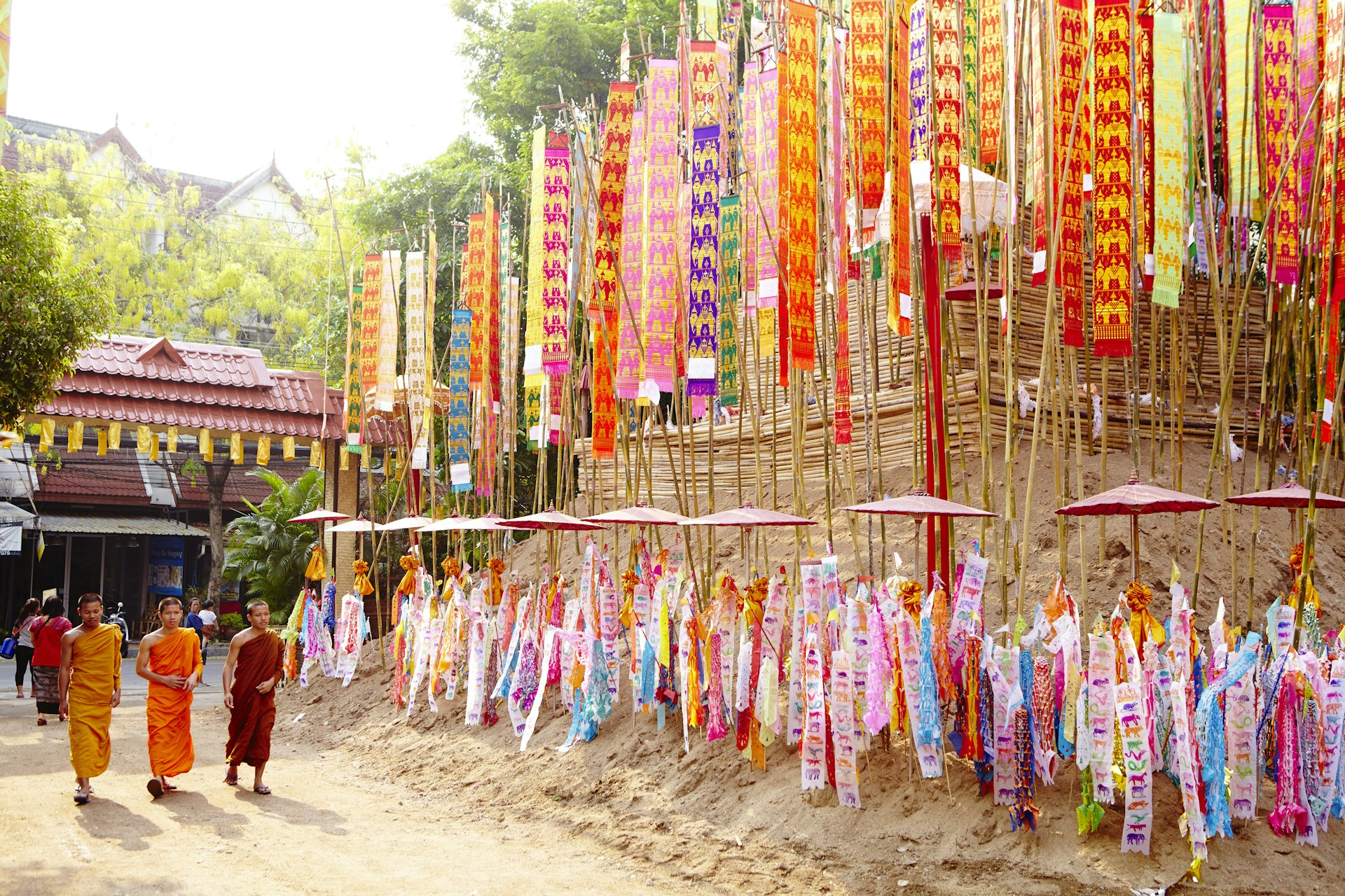 Young monks walk in front of colorful flags at a temple. 