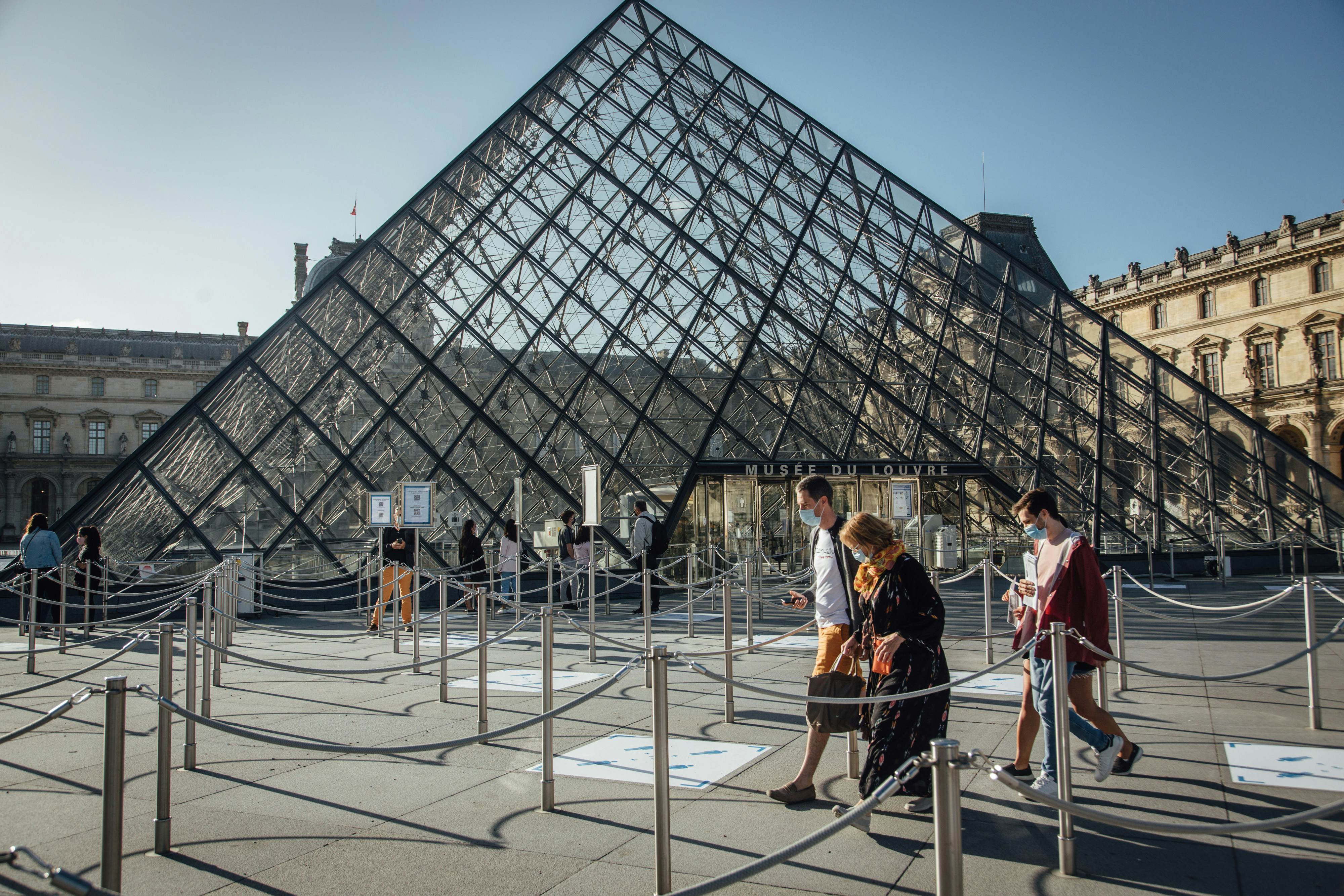 Tourists wearing protective face masks pass between queuing cordons at the Louvre Museum ahead of reopening in Paris, France, on Monday, July 6, 2020. The Louvre had 9.6 million visitors last year.