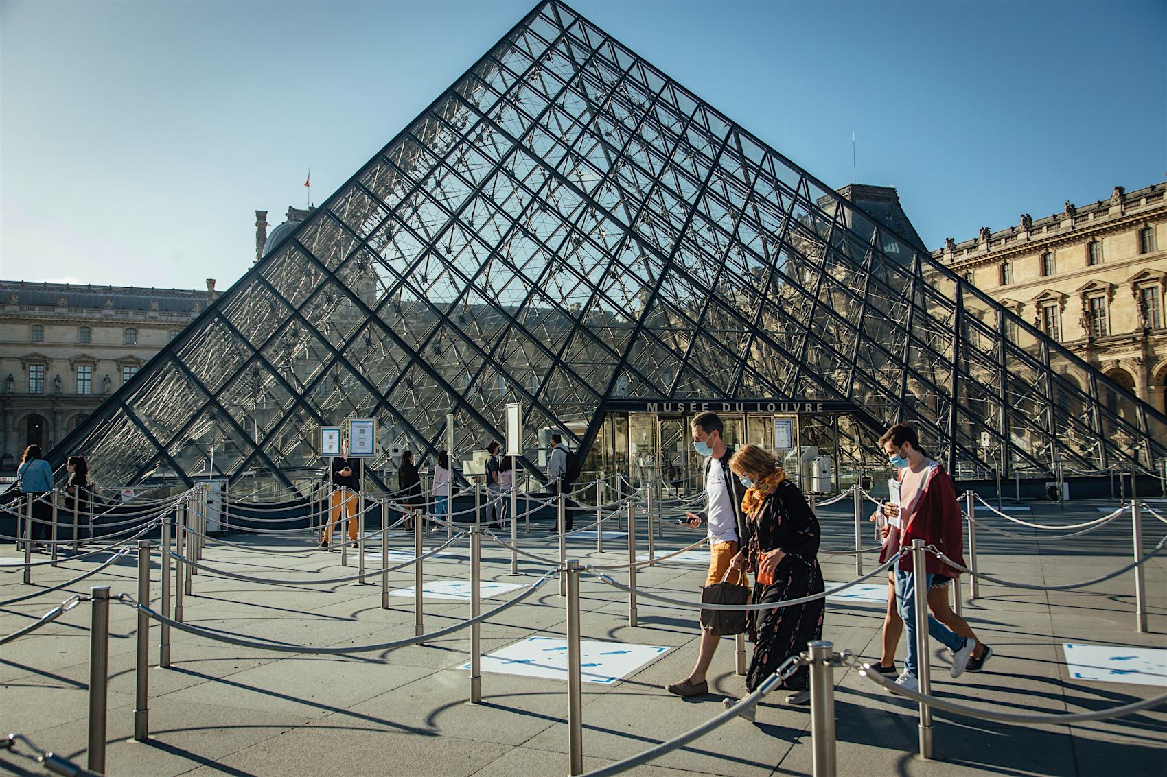 Tourists wearing protective face masks pass between queuing cordons at the Louvre Museum ahead of reopening in Paris, France, on Monday, July 6, 2020. The Louvre had 9.6 million visitors last year.