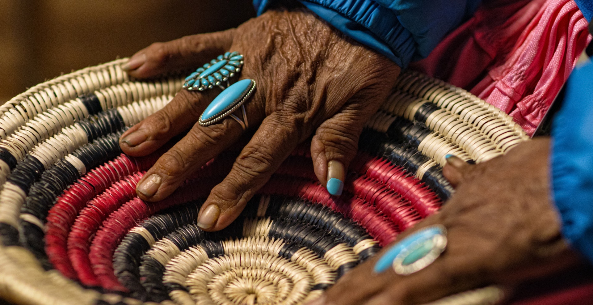 A Navajo woman wearing turquoise rings on her fingers touches a woven basket