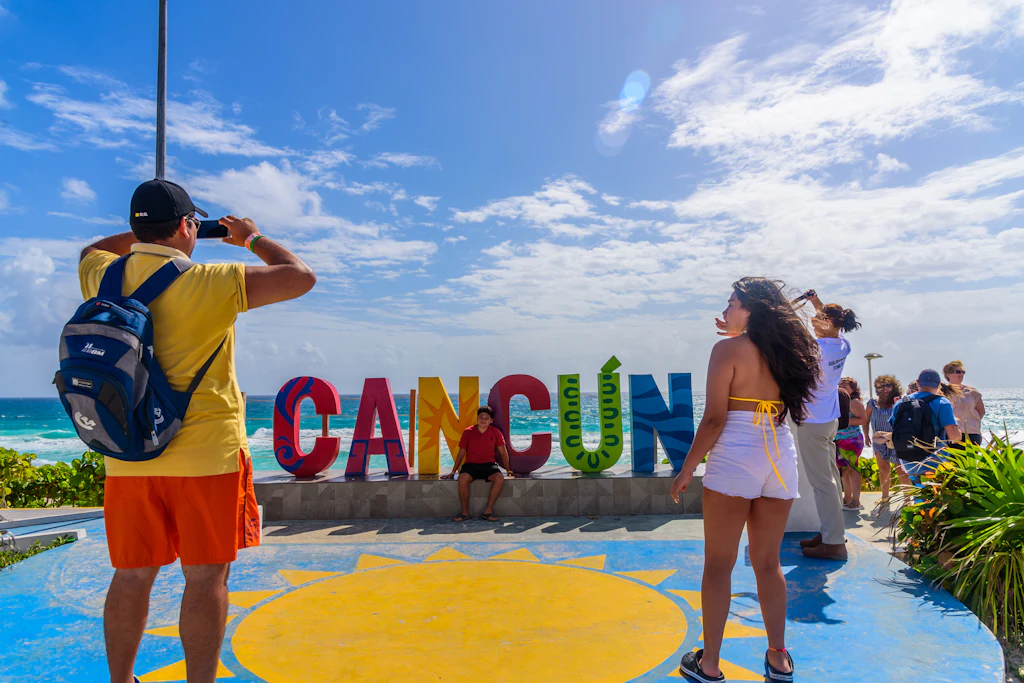 Tourists in front of the Cancun sign at Playa Delfines in Mexico Tourists in front of the Cancun sign at Playa Delfines in Mexico