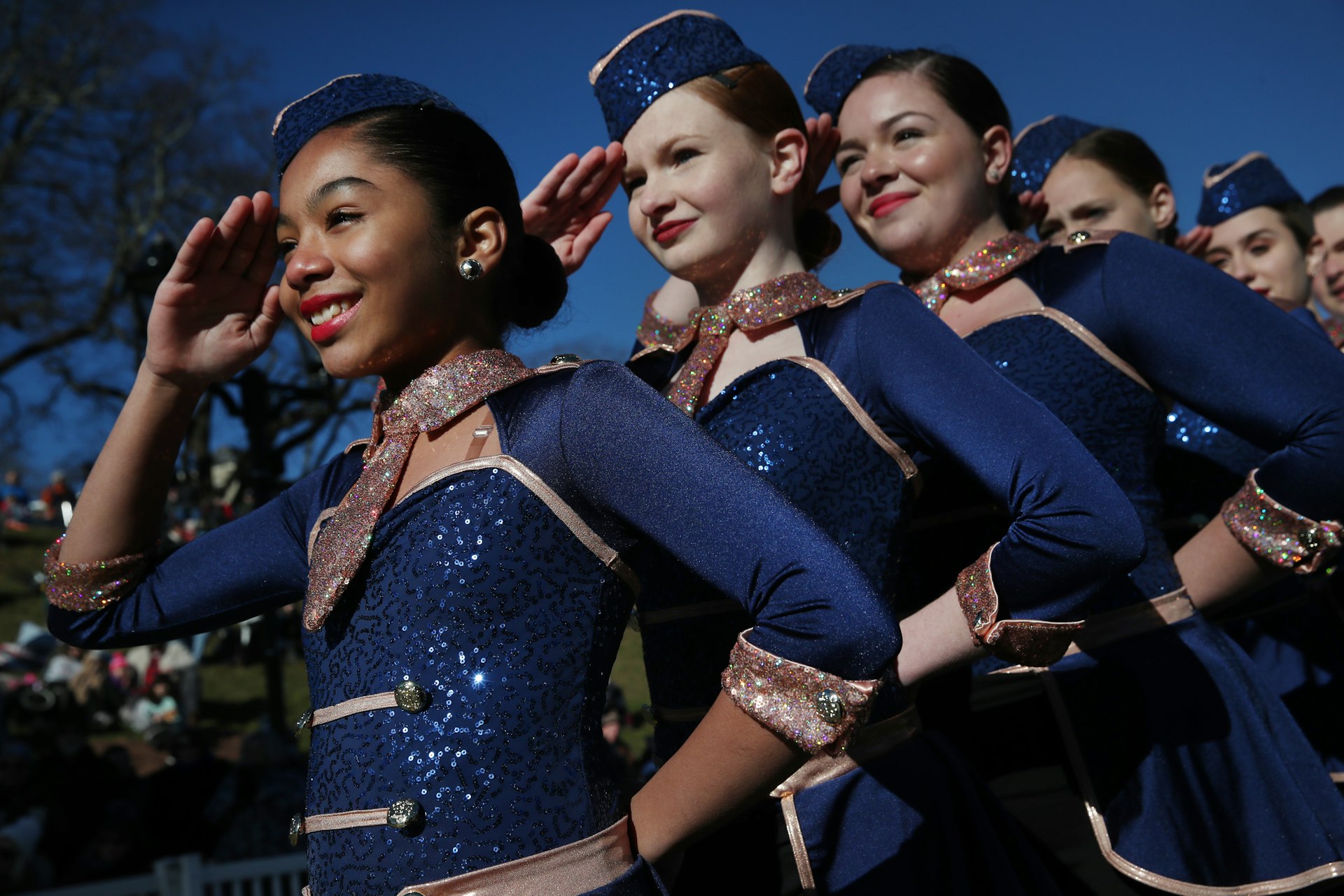A group of young dancers in sparkling tops and army hats salute as they stand in a line at the Plymouth Thanksgiving Parade. 