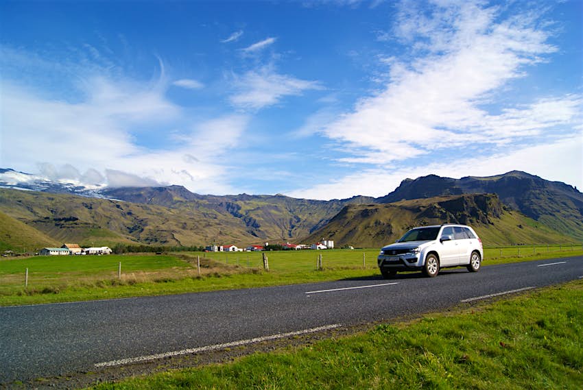 A car driving along a road, with mountains in the backgroun d