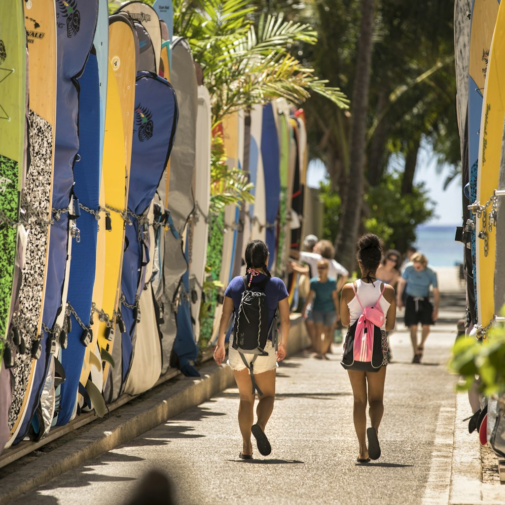 Honolulu: Tourists walk by a surfboard lined alley off the commercial shopping district of Kalakaua Avenue by Waikiki Beach.  Surfboards are locked up here when not in use.