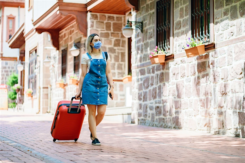 tourist Young woman wearing medical mask and walking with suitcase on the street