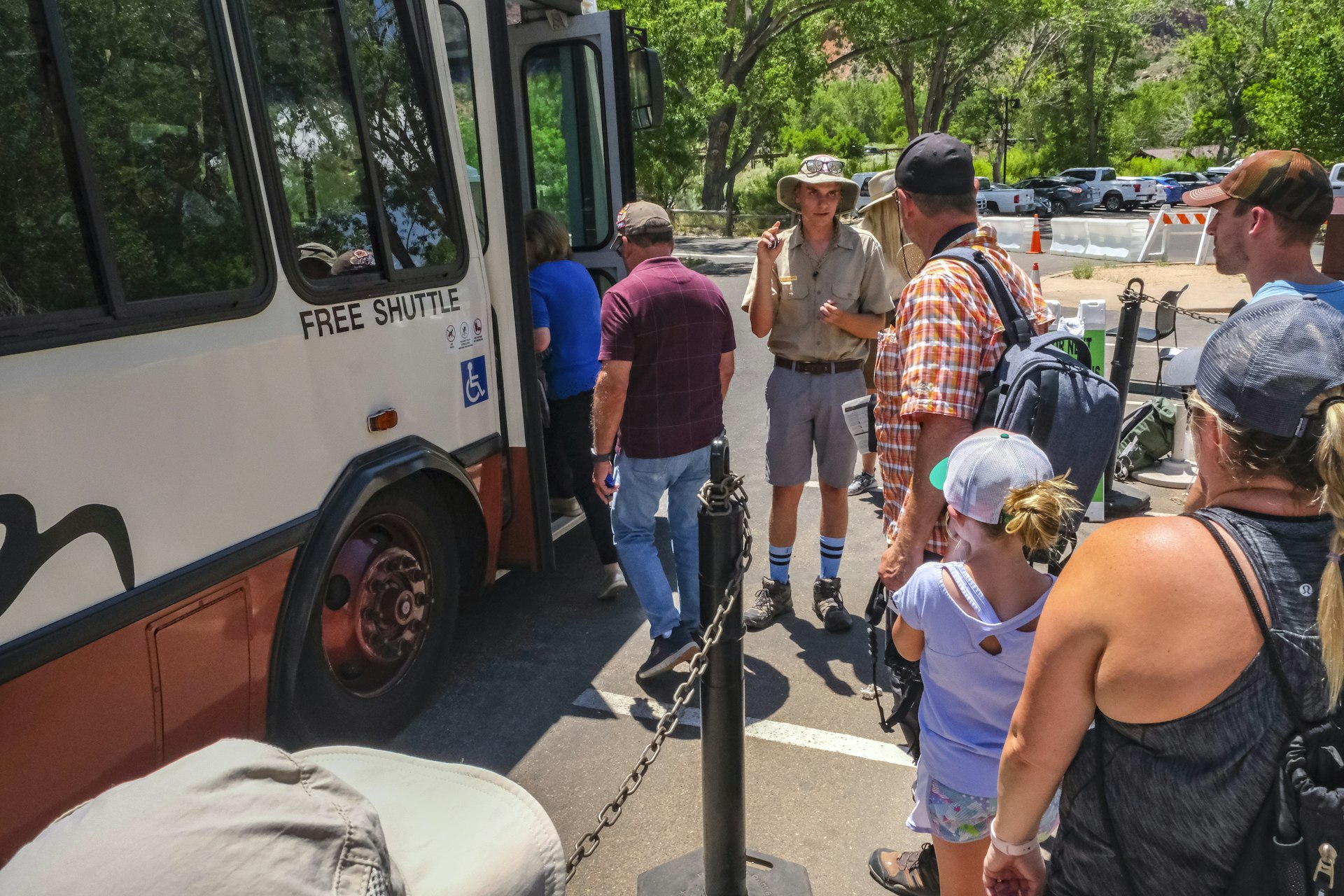 A park ranger stands next to a shuttle bus as people wait to board at Zion National Park. 