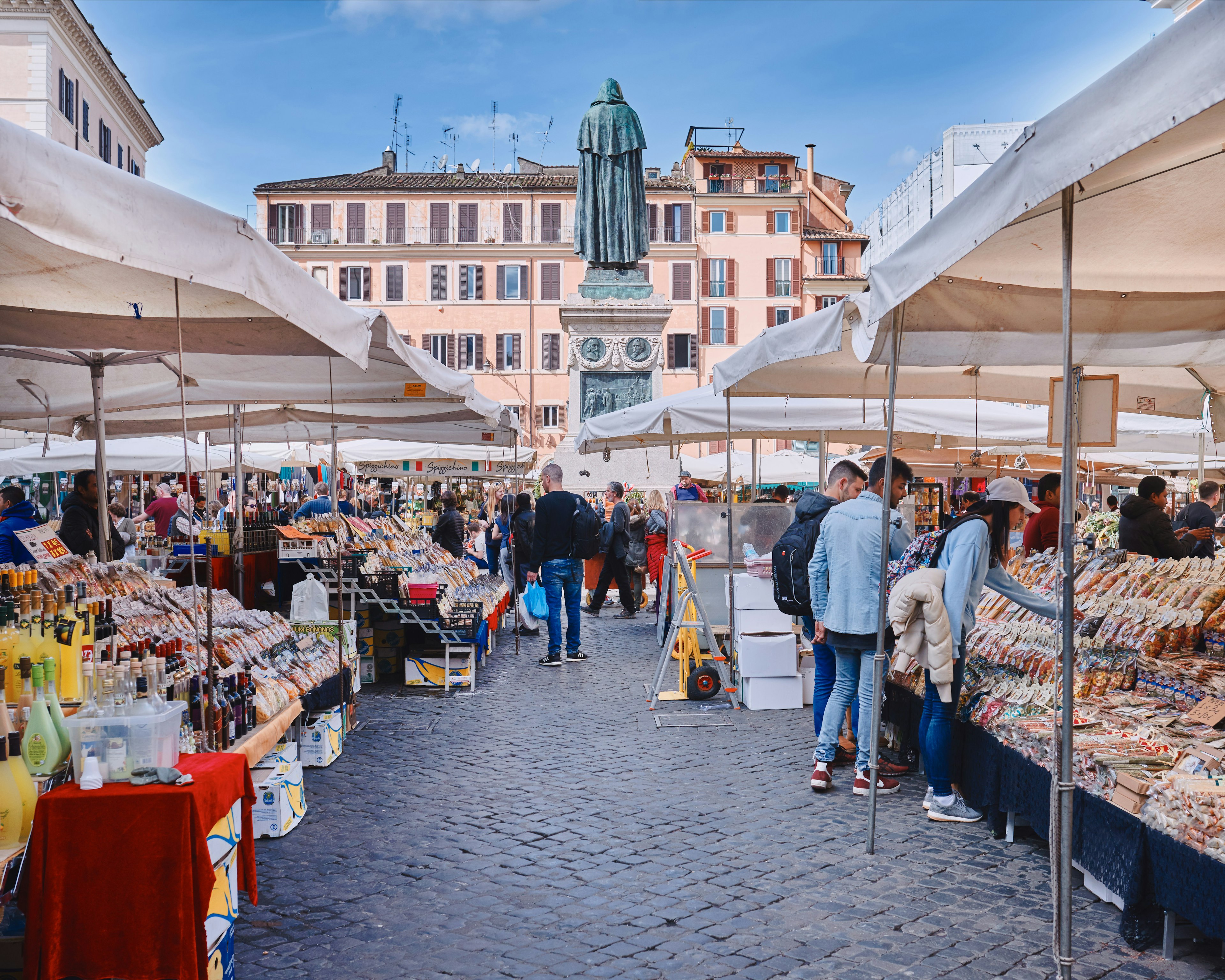 People browse market stalls that fill a square in a city