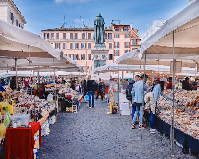 People browse market stalls that fill a square in a city