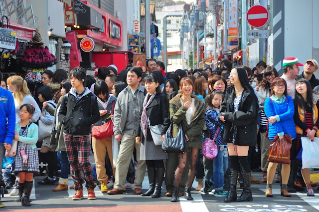 People, mostly youngsters, wait to cross a road in a busy city
