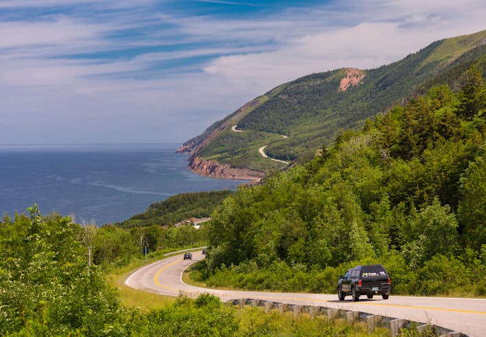 A road curves through the green hillsides of Cape Breton Highlands National Park, Nova Scotia.