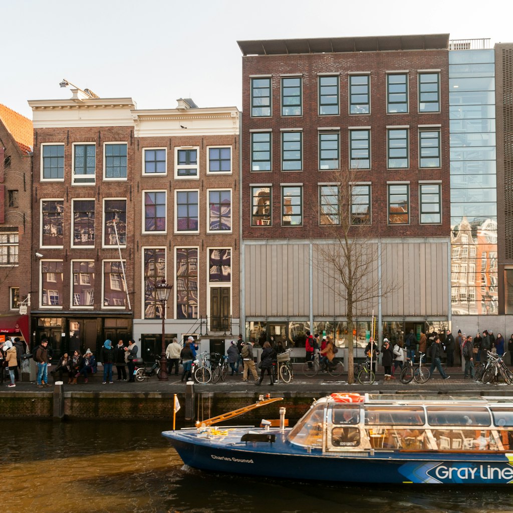February 13, 2018: Queue of people waiting to enter the Anne Frank museum house, with a passing tour boat on the canal.