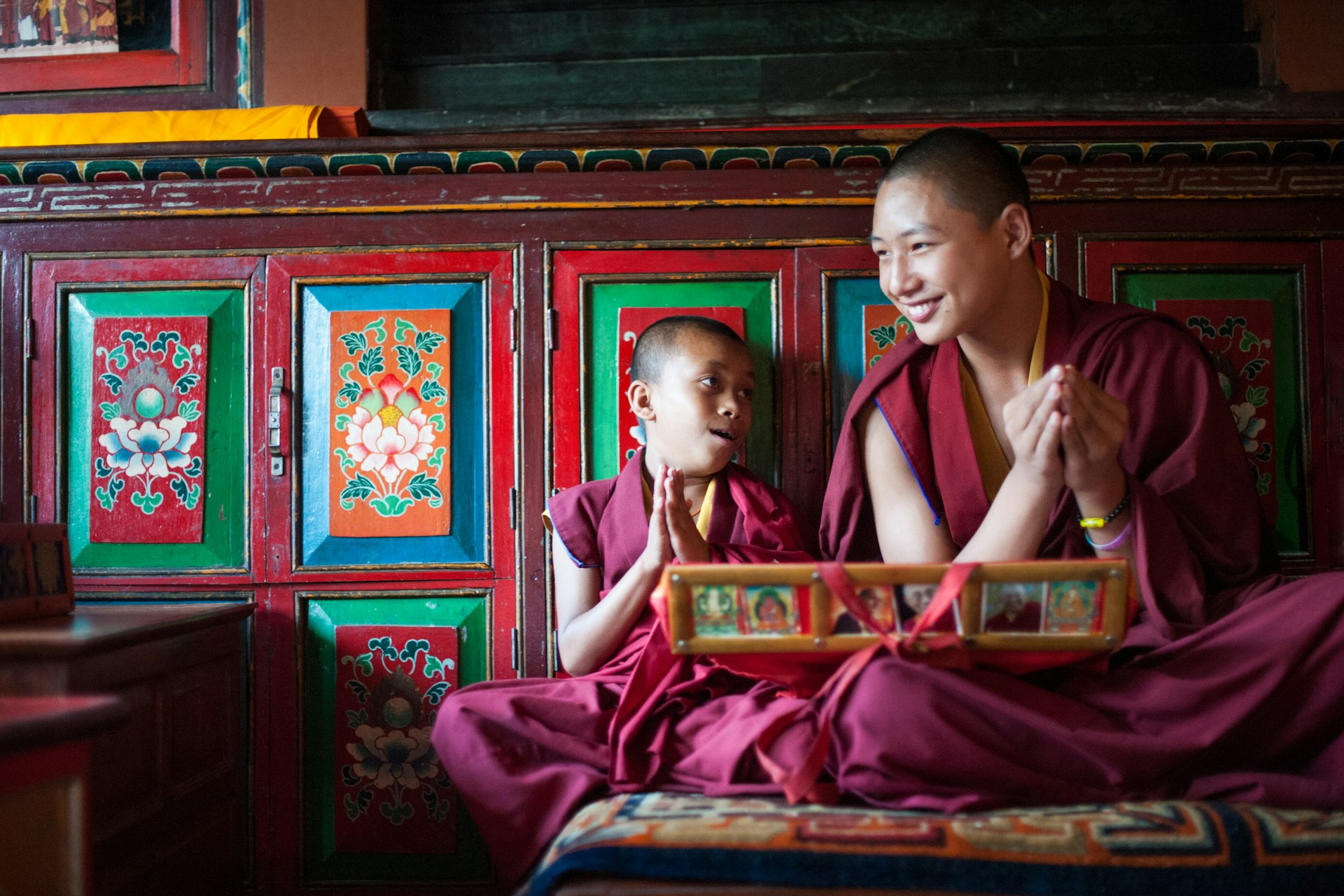 Unidentified buddhist monks, wearing red robes, pray in Bodhnath monastery, Kathmandu. One of the monks is just a boy, while the other is a grown adult man.