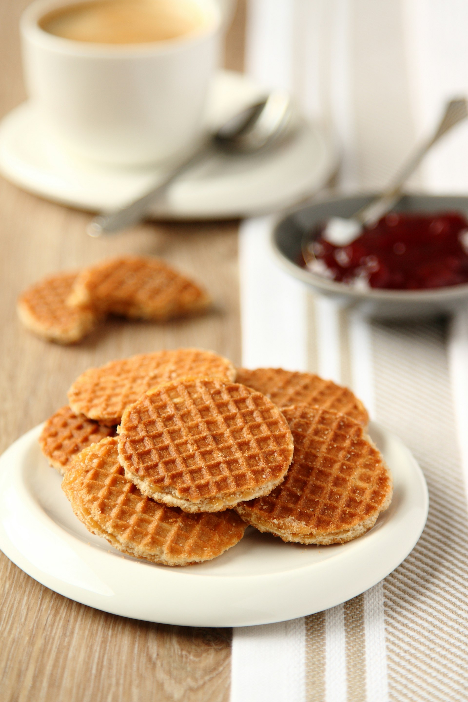 Mini stroopwafels (syrupwaffles) on a plate with cup of coffee and jam