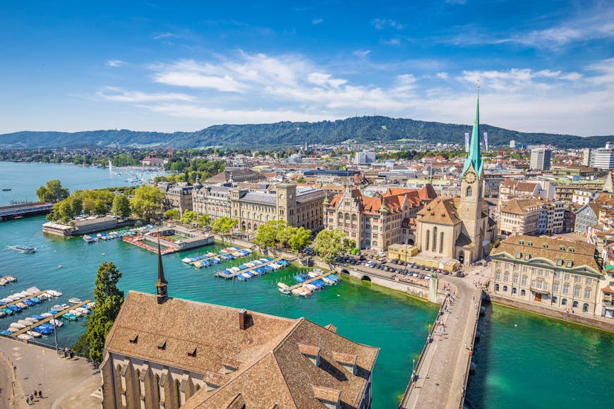 An aerial view of historic Zurich city centre on a sunny day with the famous Fraumunster Church and river Limmat in the foreground.