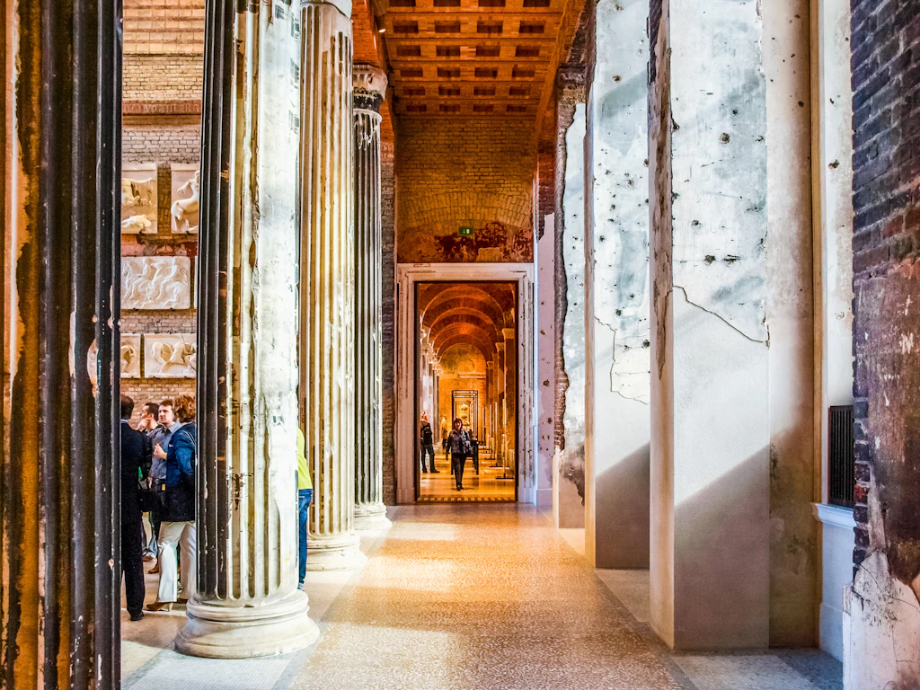 Neues Museum, Berlin Interior shot within a museum, showing a long corridor lined with Roman-columns to the left and square cracked and marked pillars to the right