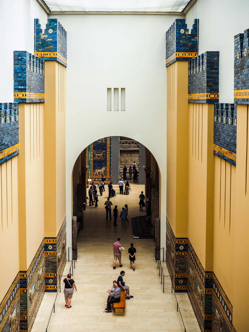 Visitors explore the Babylon Walls exhibit inside the Pergamonmuseum, Museumsinsel. The hallway has high ceilings and many people stare at the exhibits lining the walls.