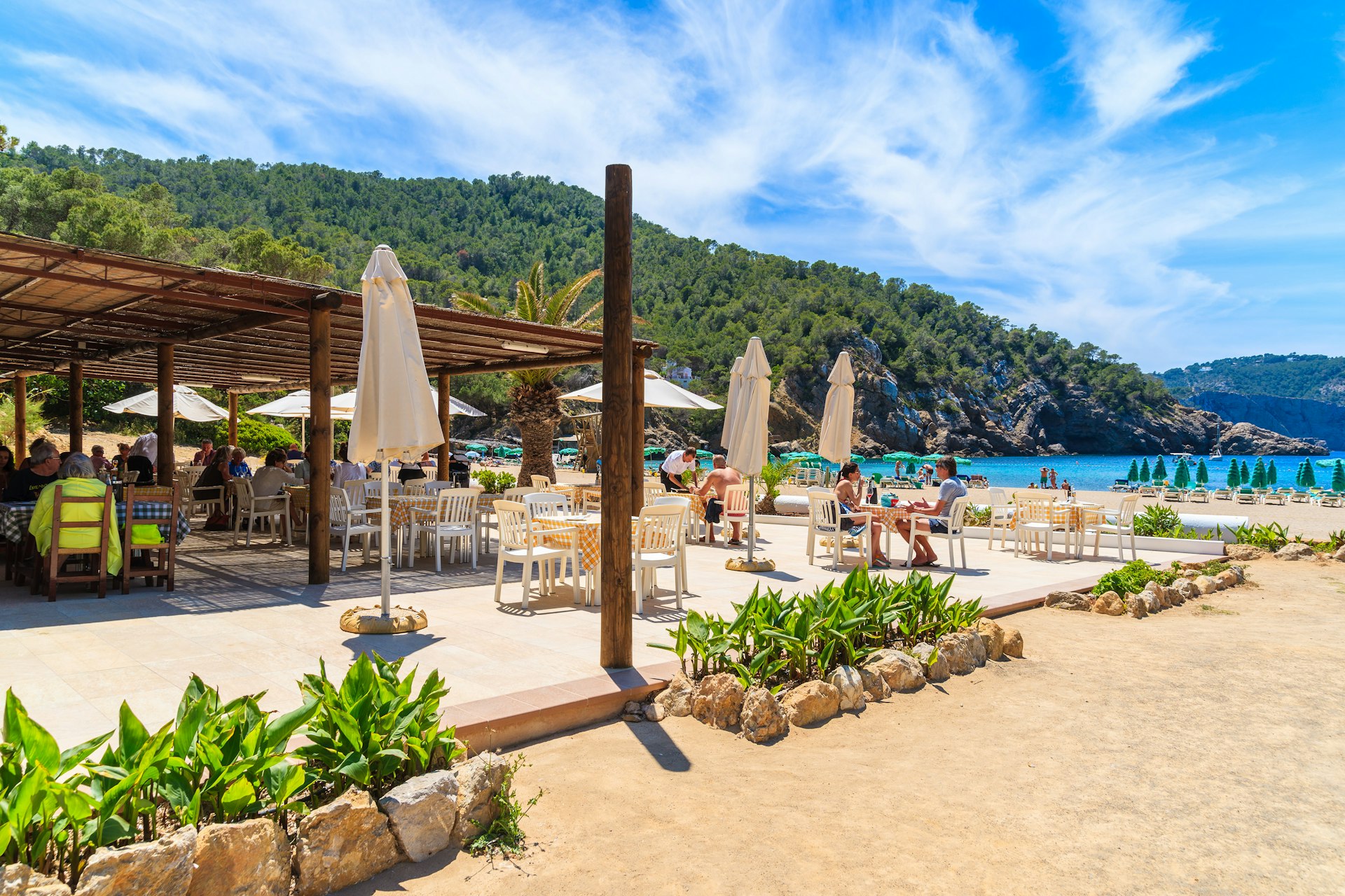 People sitting at restaurant tables on a terrace at Cala Benirrás beach on Ibiza