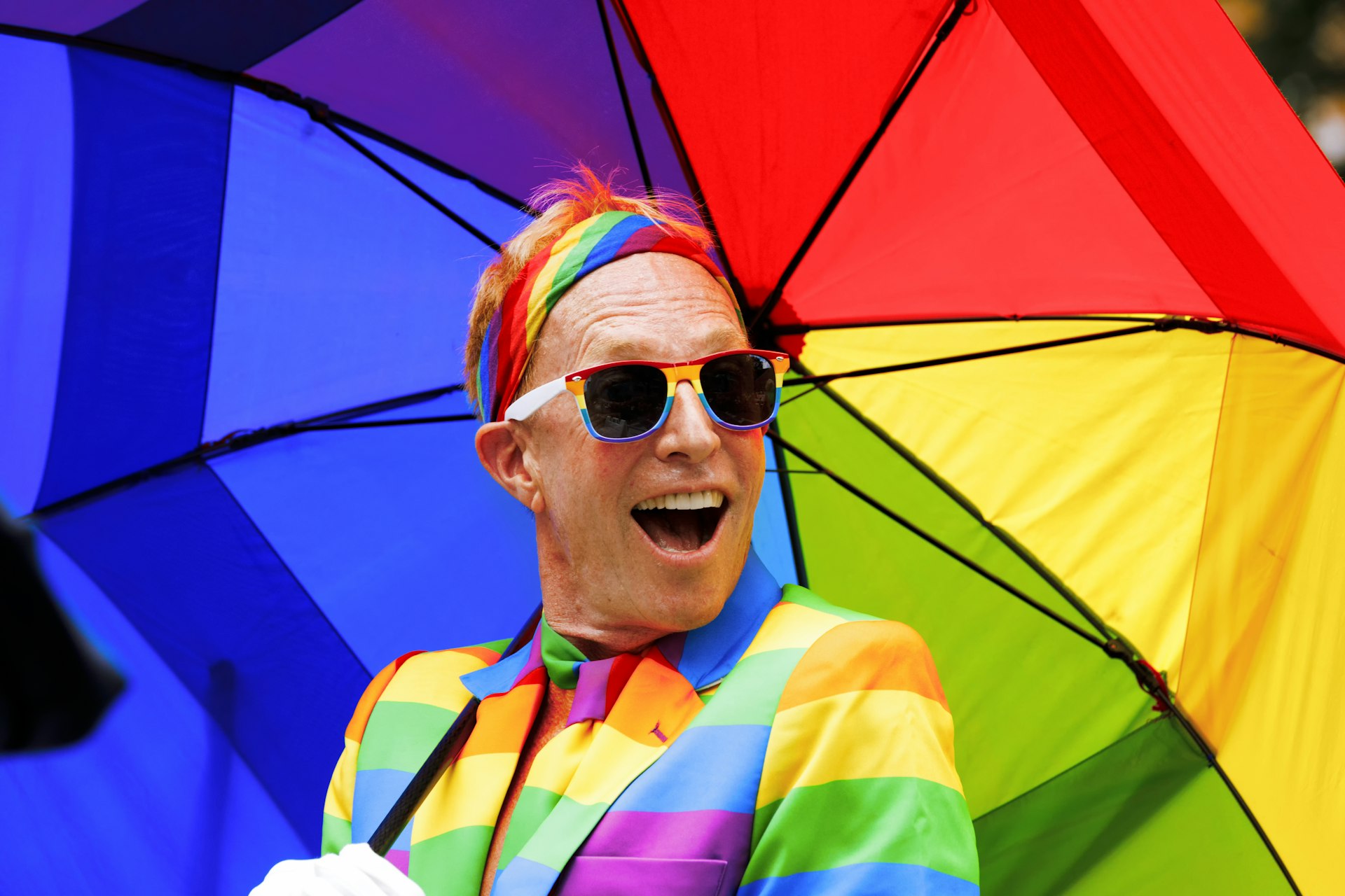 A man wearing a rainbow suit and holding a rainbow umbrella in the NYC Pride March. Gay Pride events occur throughout the month of June, culminating with the March along 5th Avenue