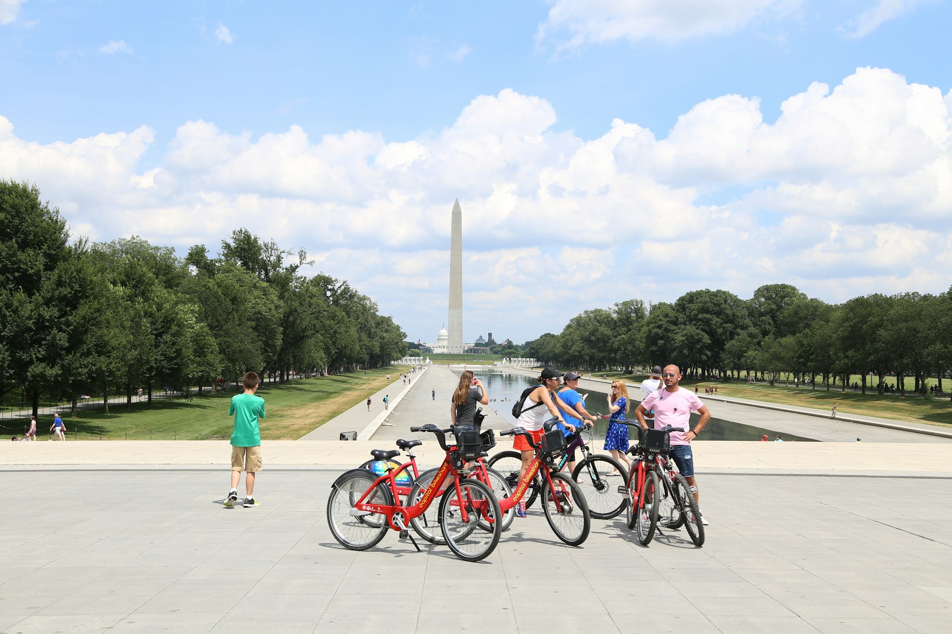 A group of people on bikes take a break while biking around the National Mall in Washington, DC. In the background you can see the Washington monument