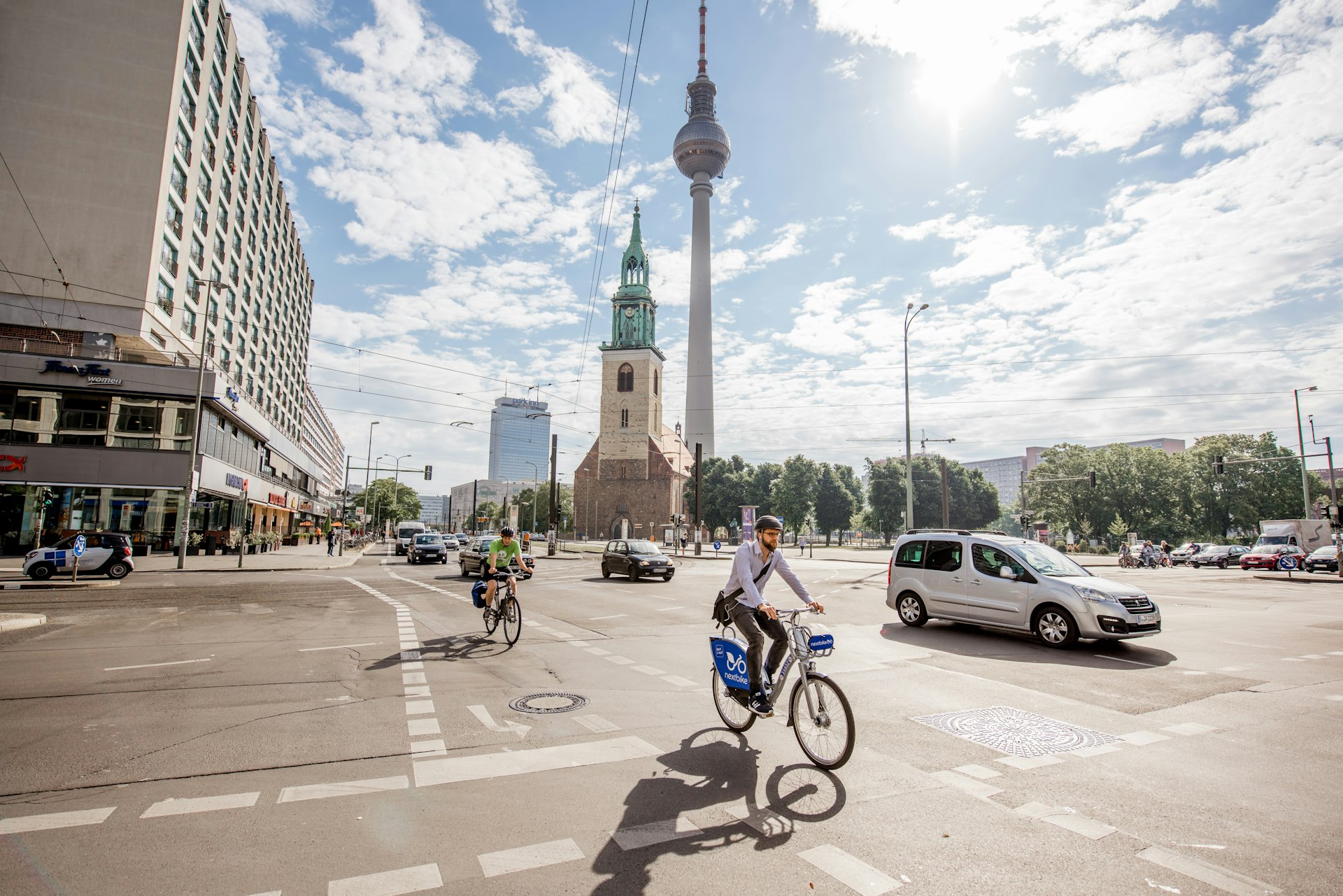 Cyclists and traffic travel in front of Saint Mary's church and the television tower (Fernsehturm) in the morning