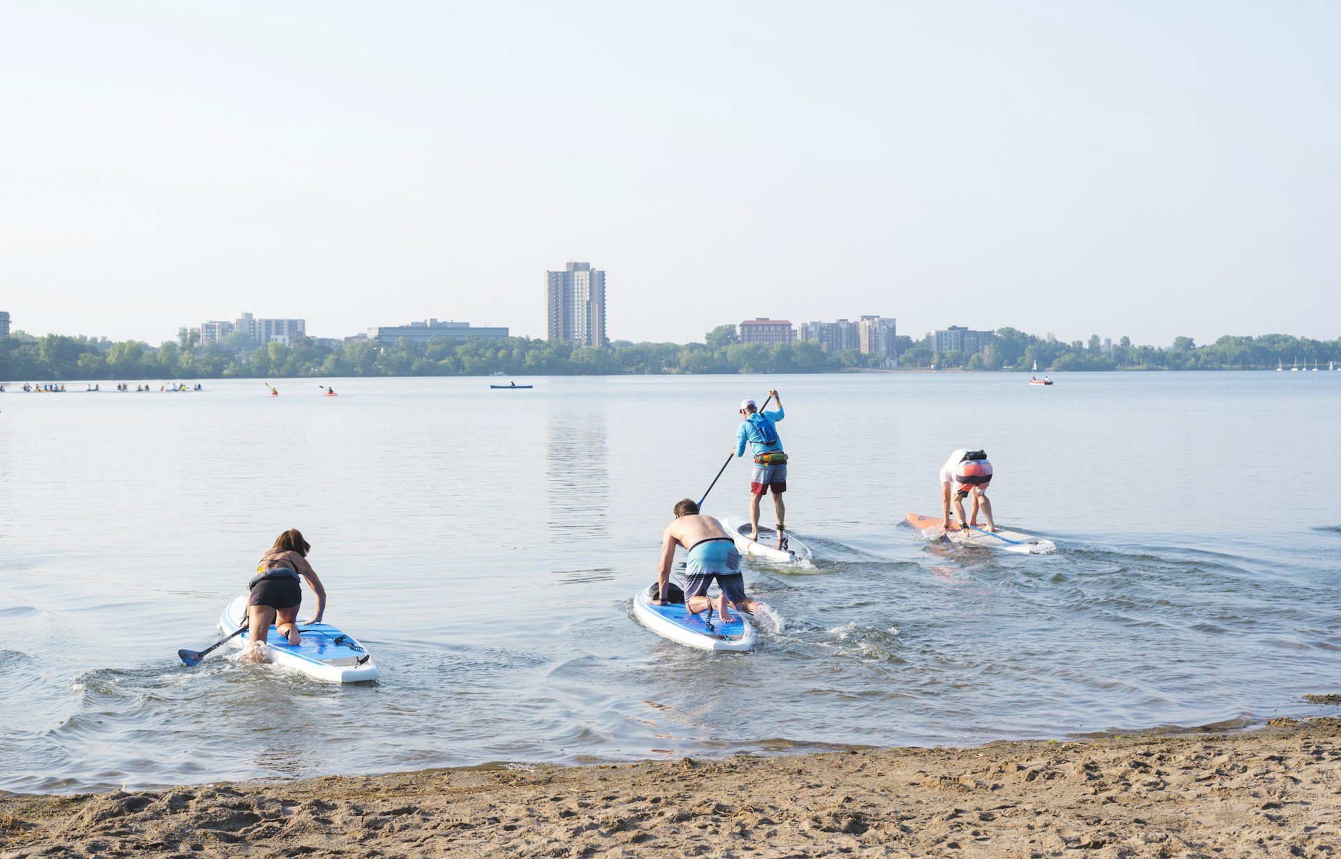 Four paddleboarders leave the sandy beach and head out onto Bde Maka Ska lake in Minneapolis, Minnesota