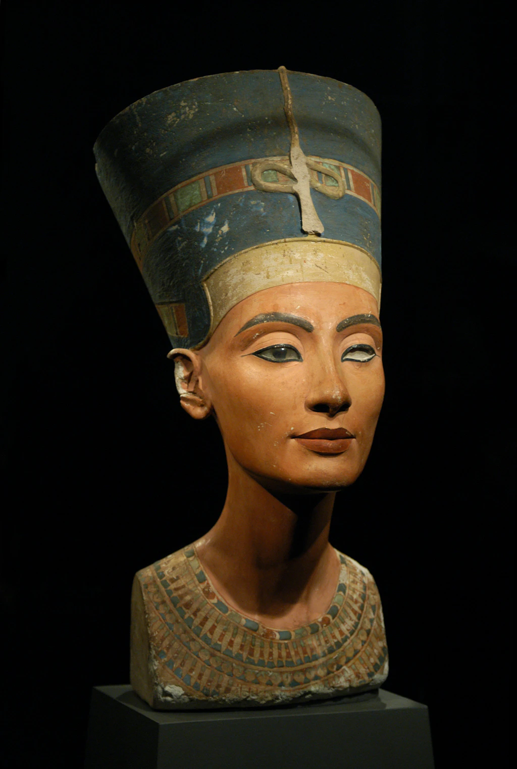 An ancient sculpture of a woman from the chest upwards. She wears a tall hat.