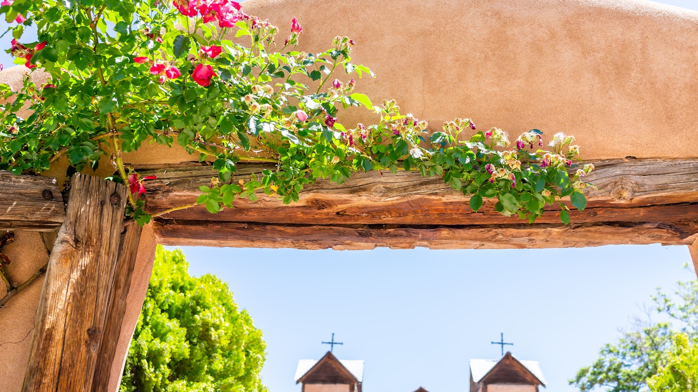 Famous El Santuario de Chimayo sanctuary church in the United States with entrance gate closeup of flowers in summer; Shutterstock ID 1476876161; your: Tasmin Waby; gl: 65050; netsuite: Online Editorial; full: Core Demand