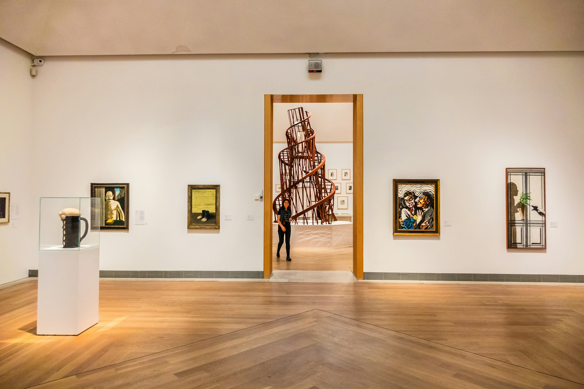 A gallery space with various pieces of modern art on the walls and a central spiral sculpture viewed through a doorway