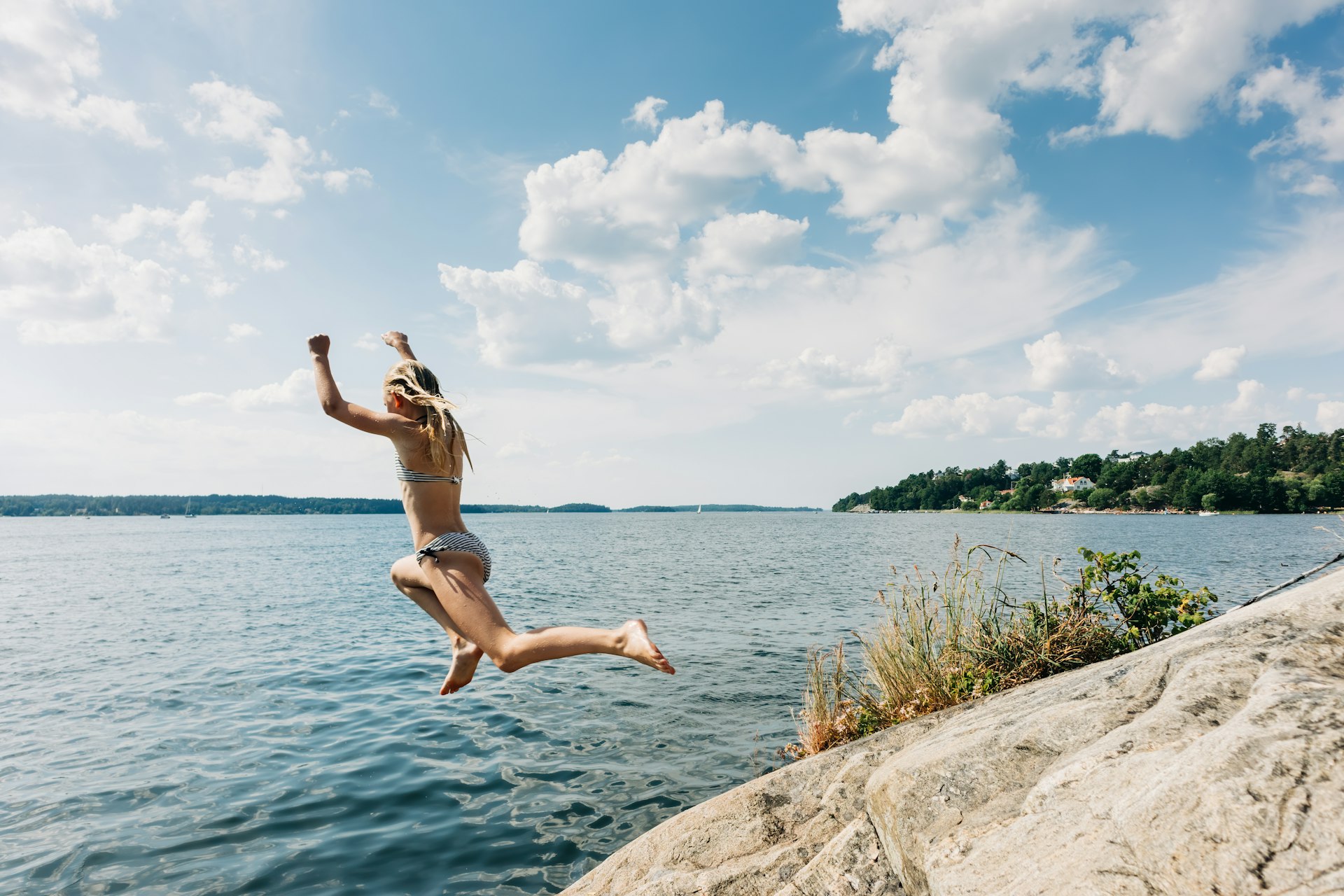 Kid jumping from cliff into water in summer