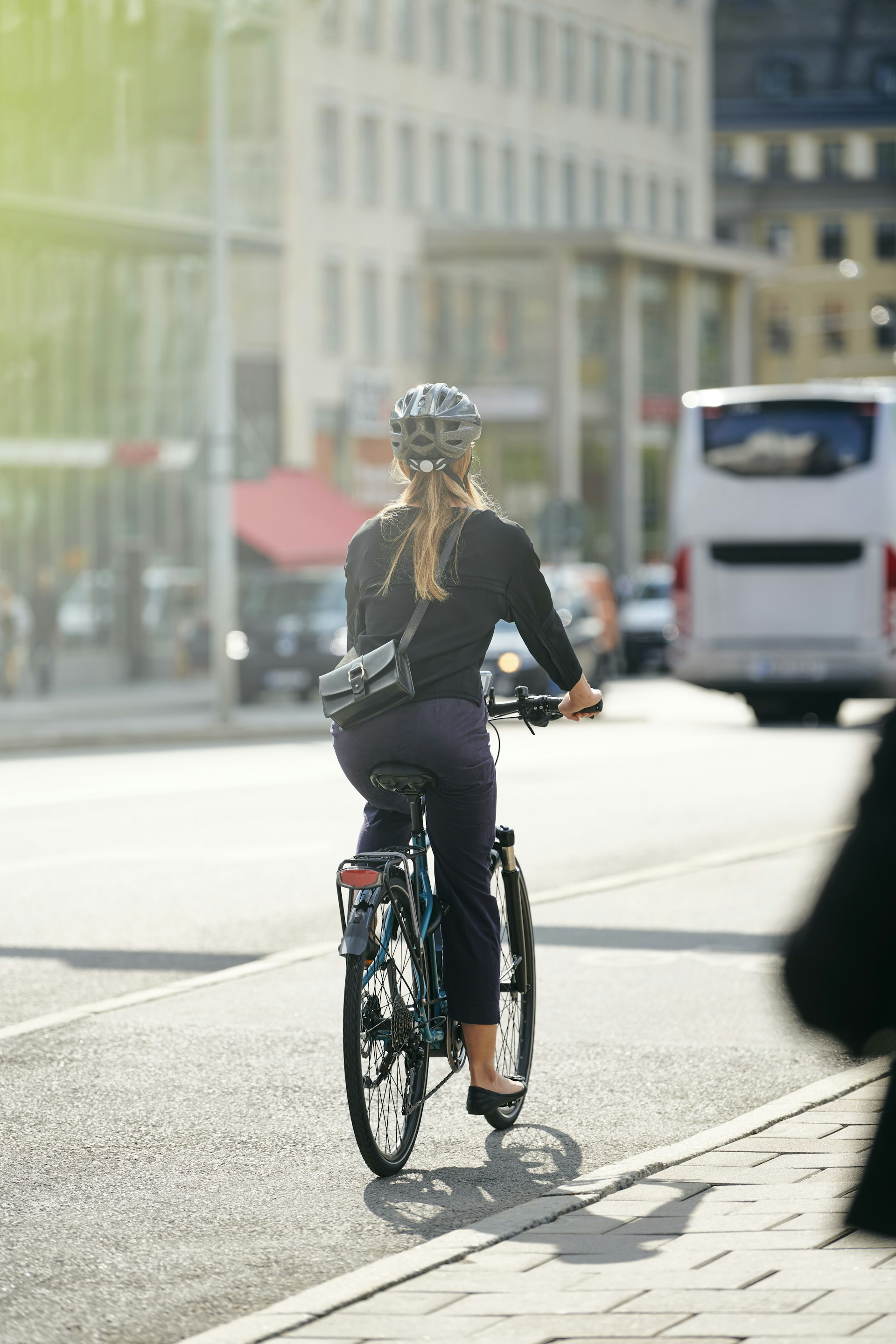 Full length rear view of young female commuter cycling on street in city