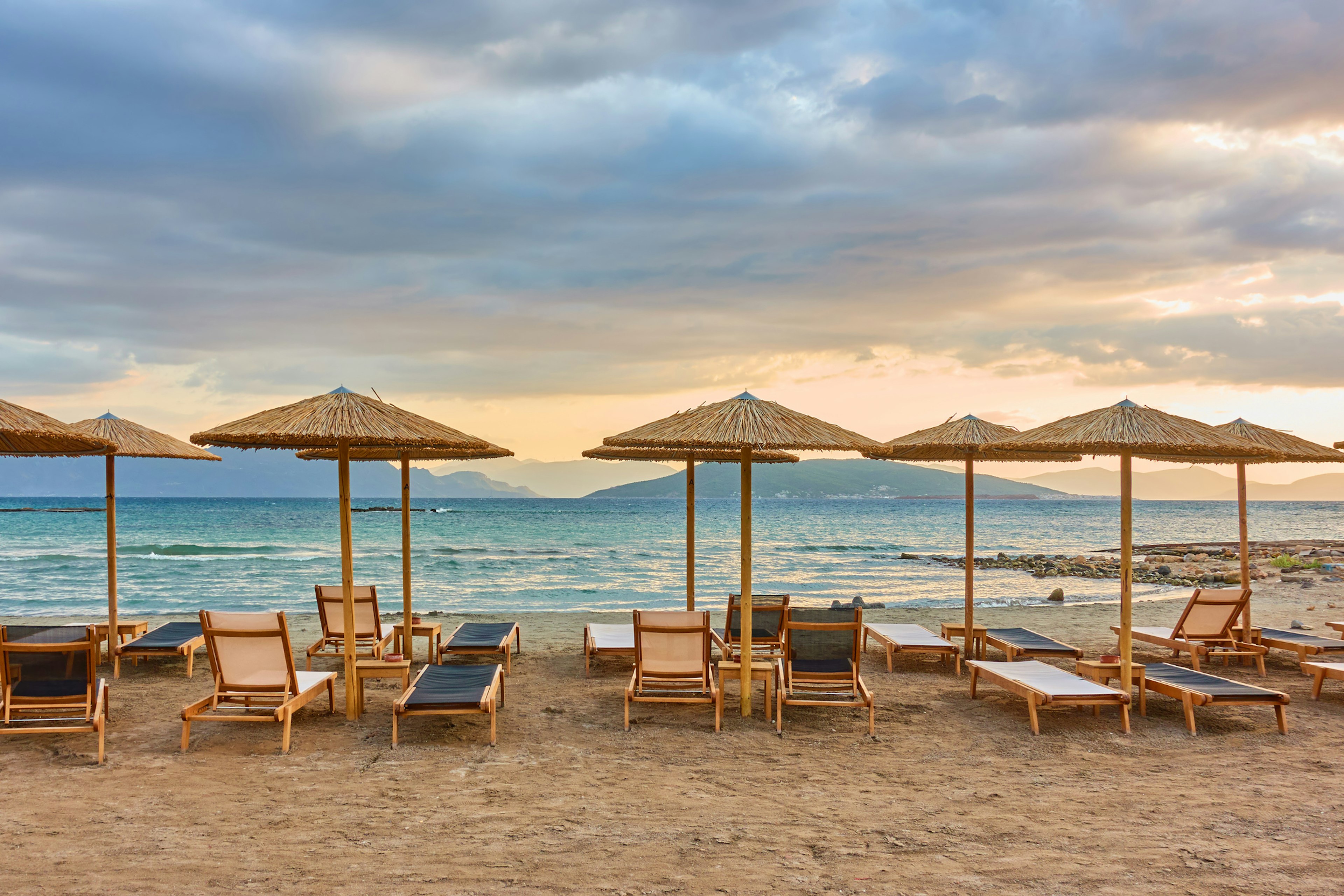 Sea beach with rows of straw parasols at sunset