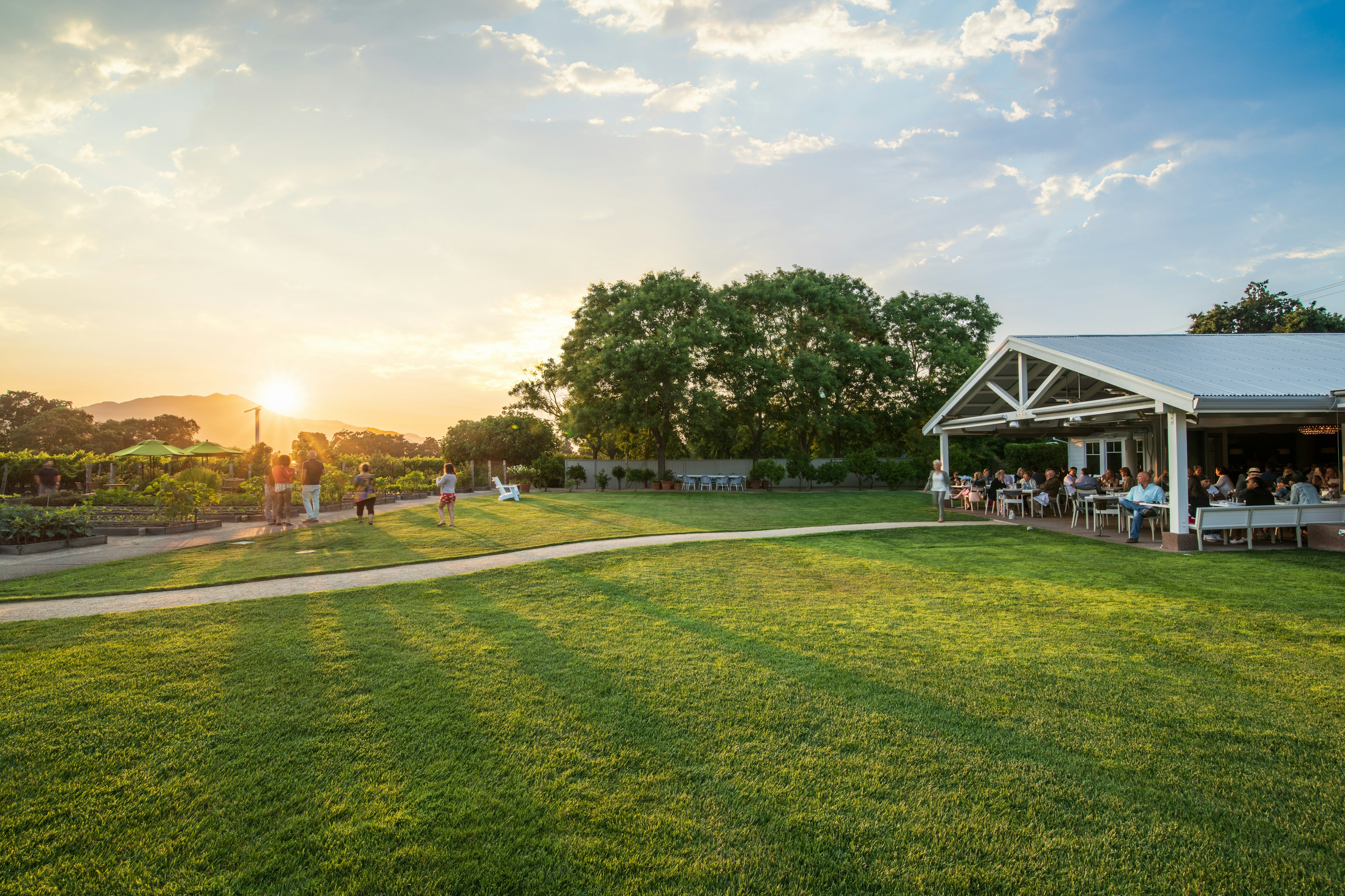 A huge covered decking area filled with diners on the edge of a lawn in a beautiful manicured garden