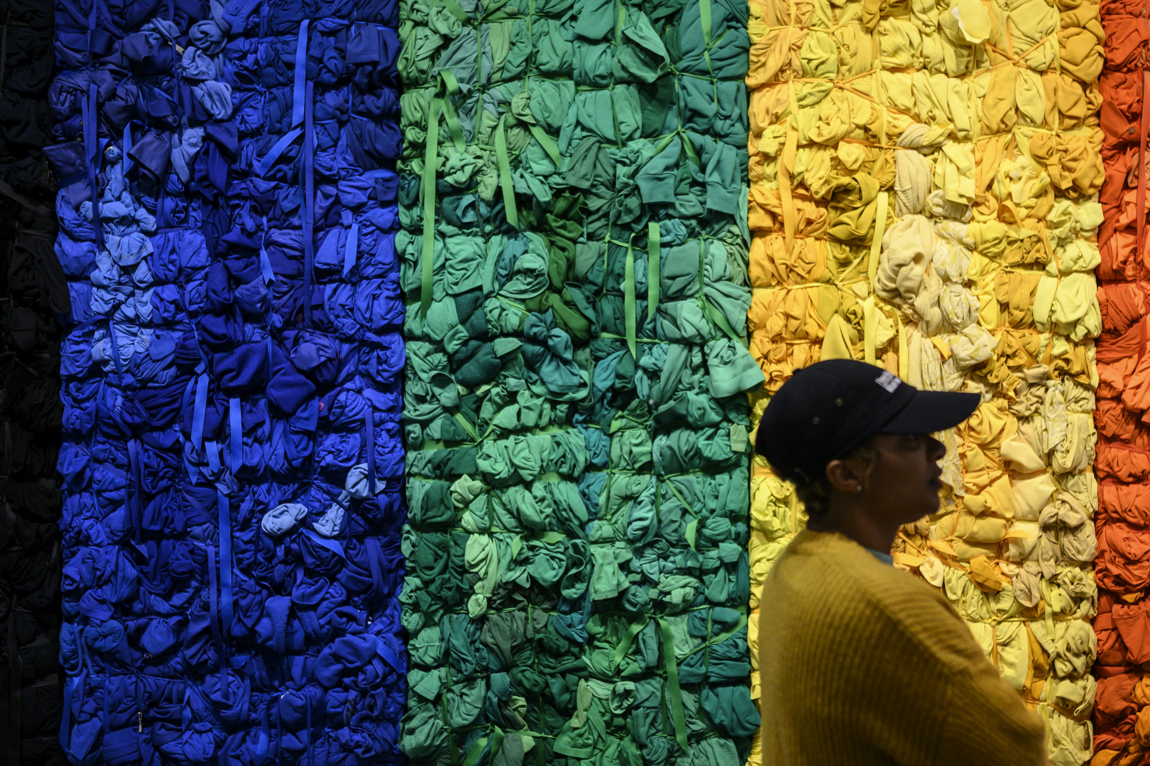 A visitor to the Baltimore Museum of Art stands in front of a blue, yellow, green and orange piece of vertical art hanging on a wall.